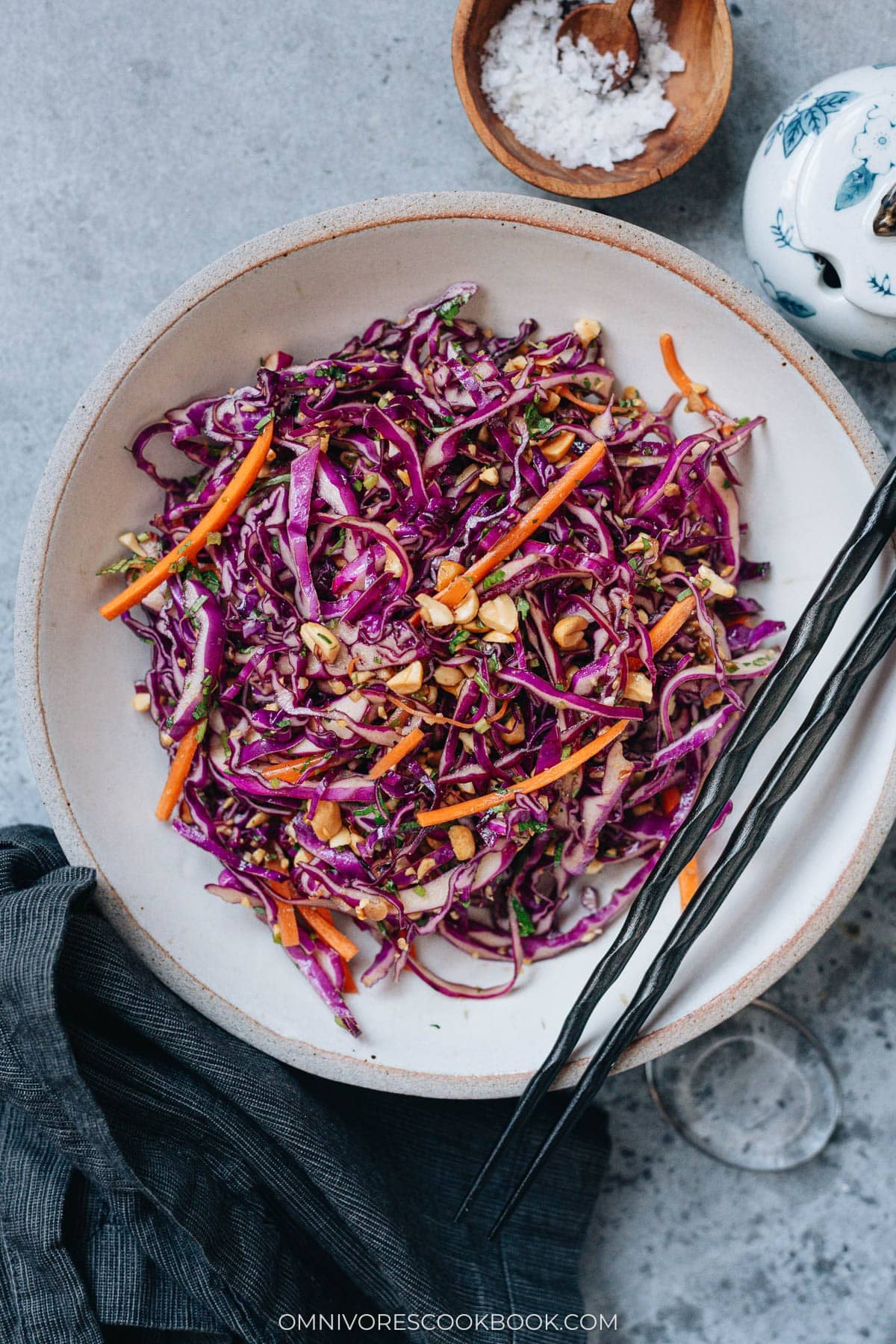Crisp Chinese coleslaw with purple cabbage, carrots, peanuts, and cilantro in a ceramic bowl with chopsticks.