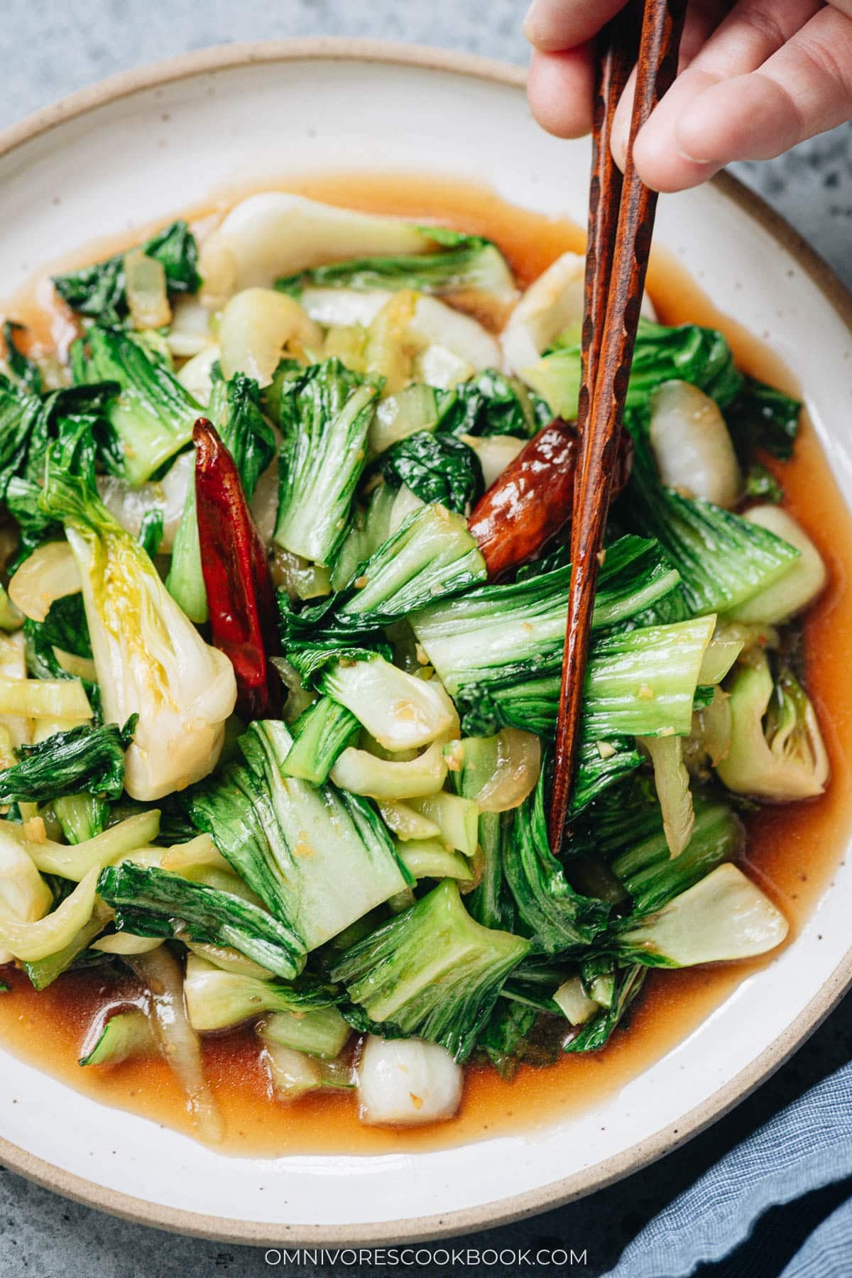 Chopsticks lifting bok choy coated in oyster sauce